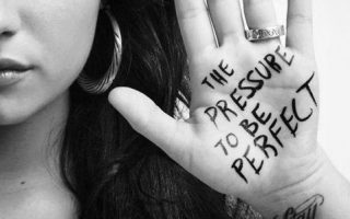 Girl with an inscription on her palm "The Pressure to be Perfect"